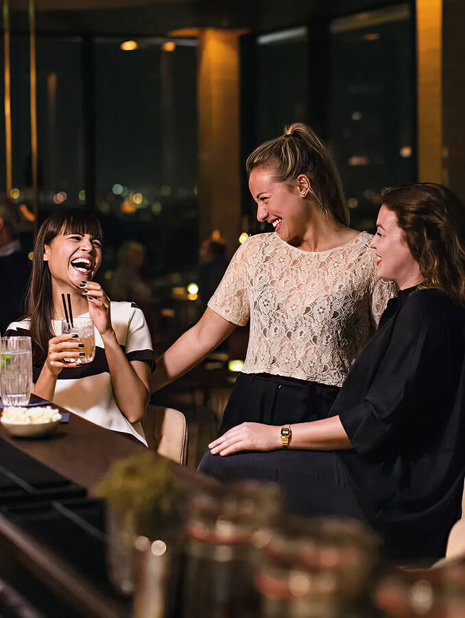 Drei Frauen an der Bar mit Cocktails und guter Laune